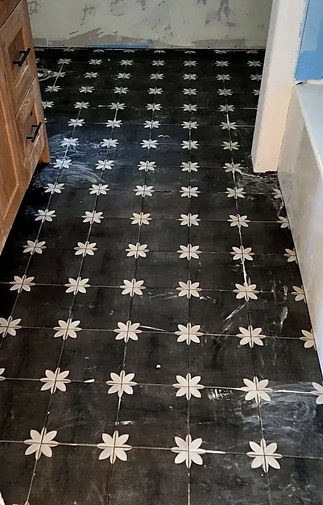 Dark patterned floor tile with a repeating cream floral motif set through a bathroom