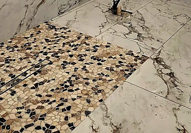 Pebble strip laid to meet a linear drain, marble mitered either side