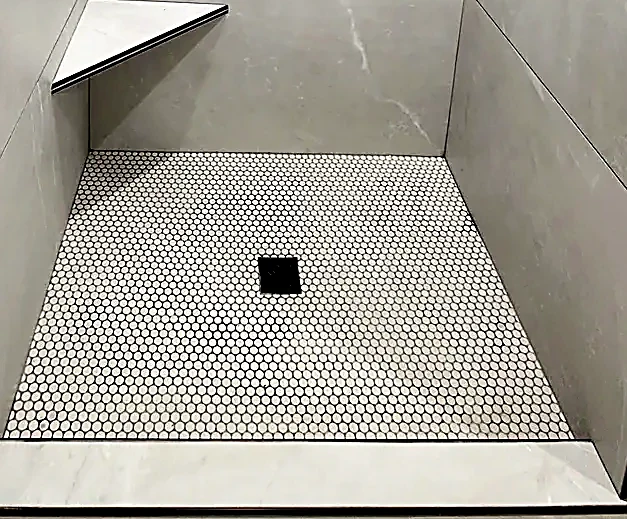Square center drain sitting flush in a penny-round pan