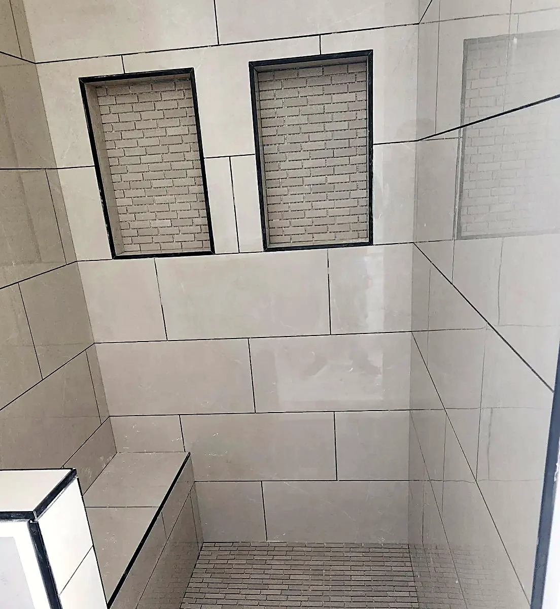 Walk-in shower in large-format gray porcelain with two recessed niches and a mosaic pan