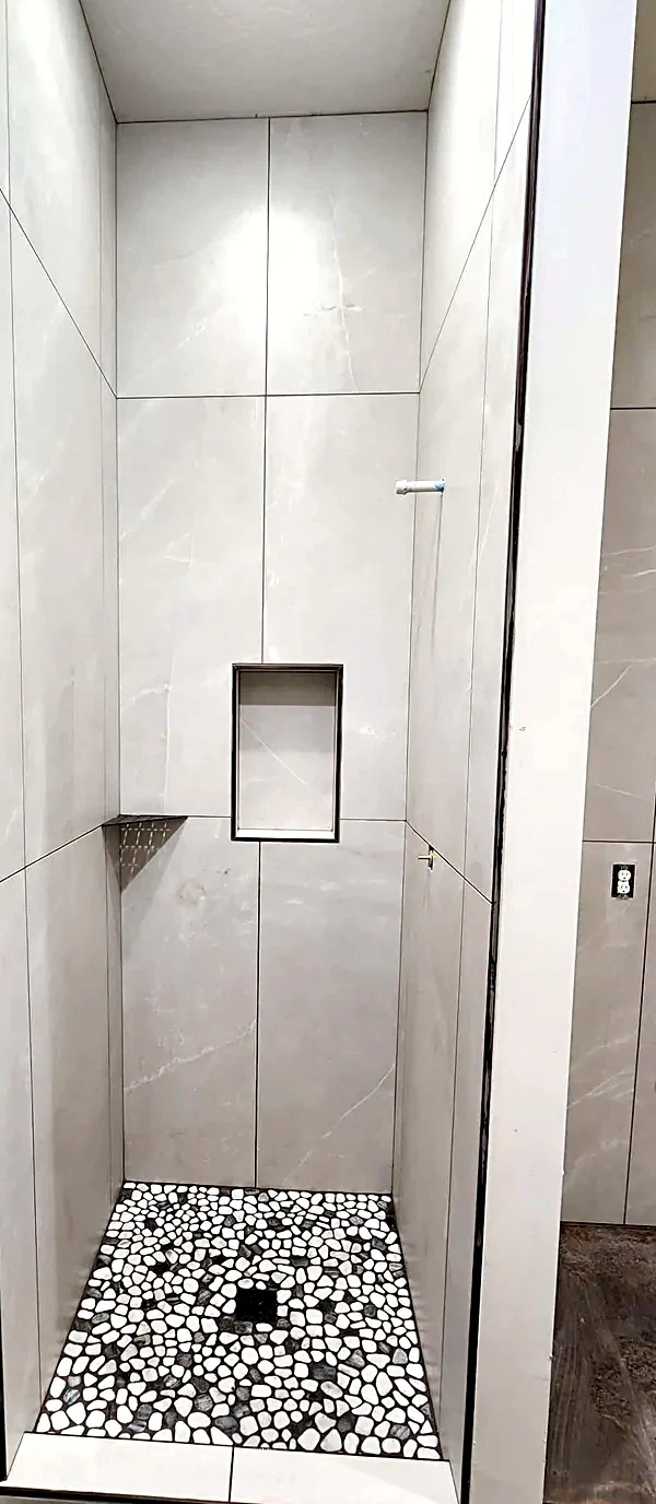 Narrow walk-in shower with pebble mosaic pan and a full-height recessed niche