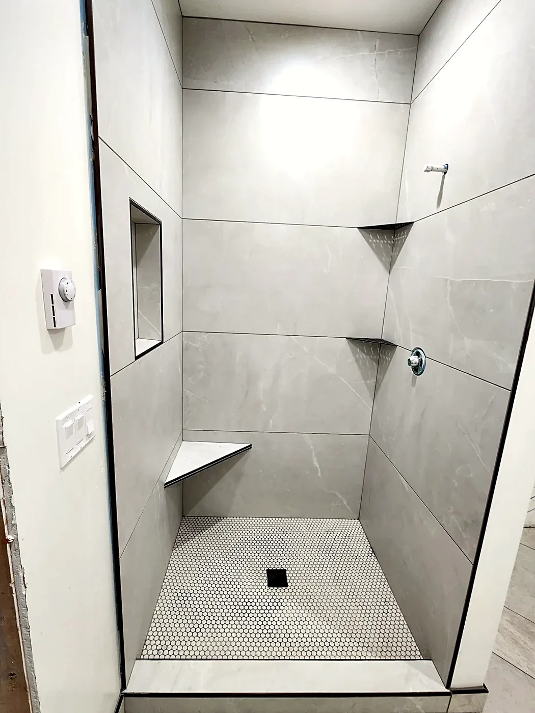 Shower pan in white penny-round mosaic with a square center drain and a folded corner bench above