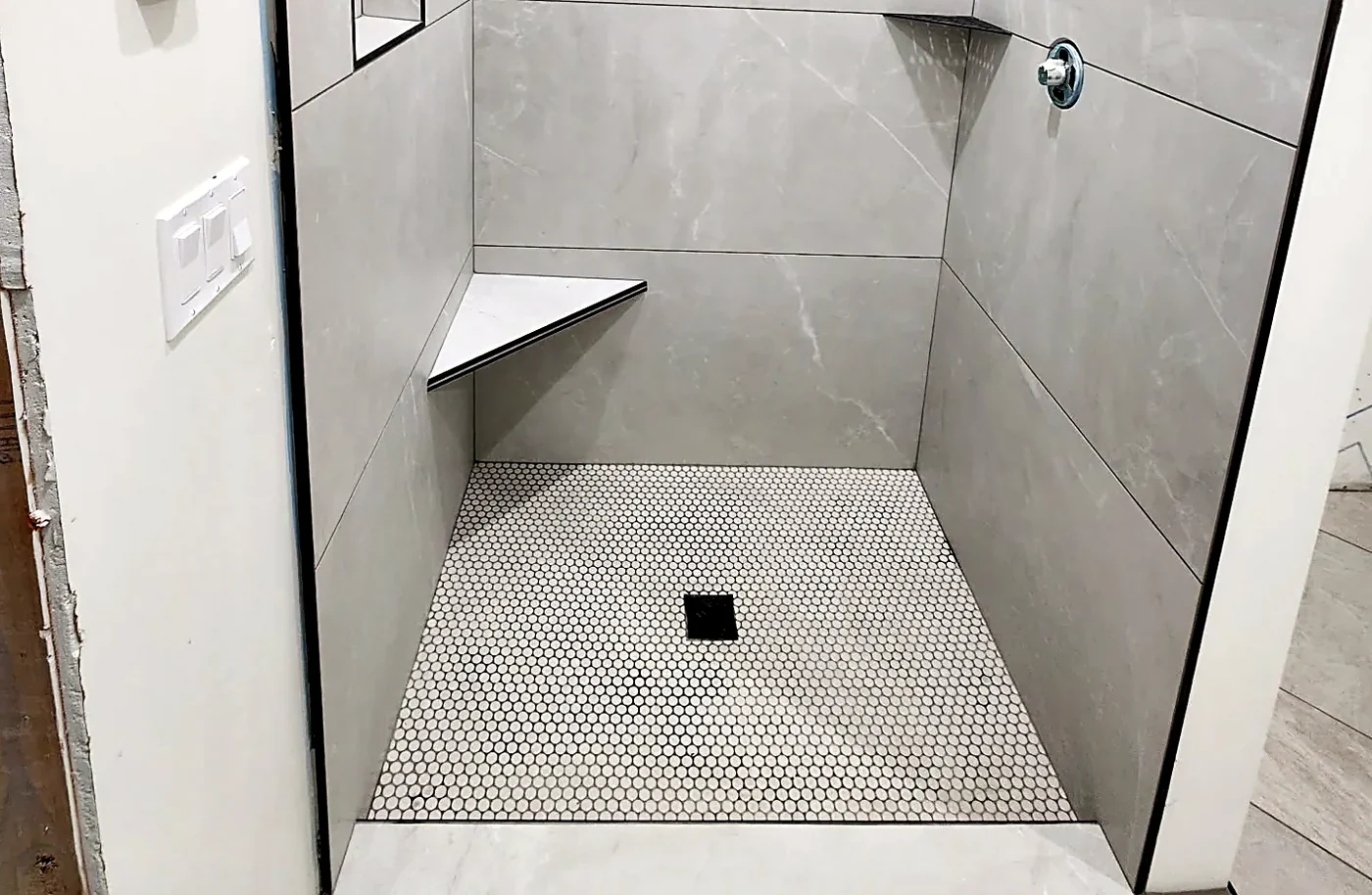 Gray porcelain shower photographed wide, penny-round mosaic pan and bench in one view