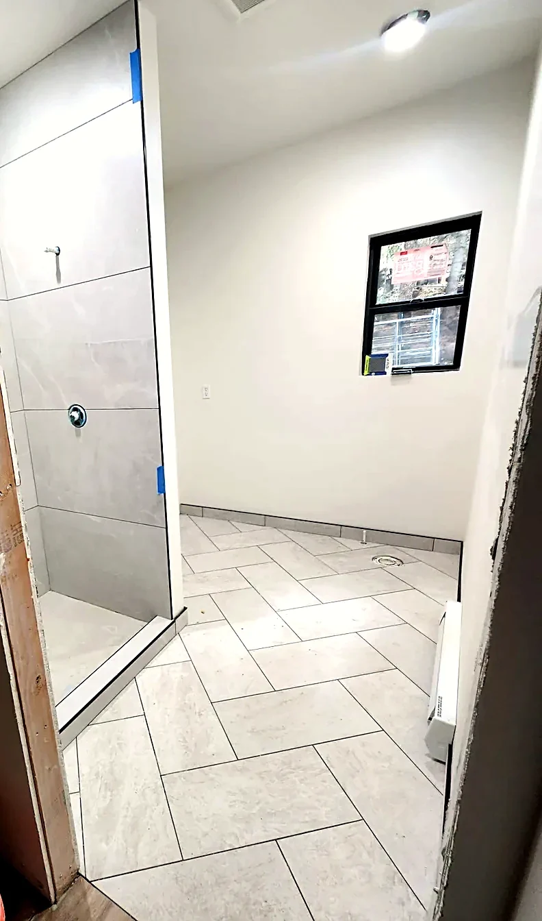 Herringbone stone-look tile floor running the length of a bathroom to the shower threshold