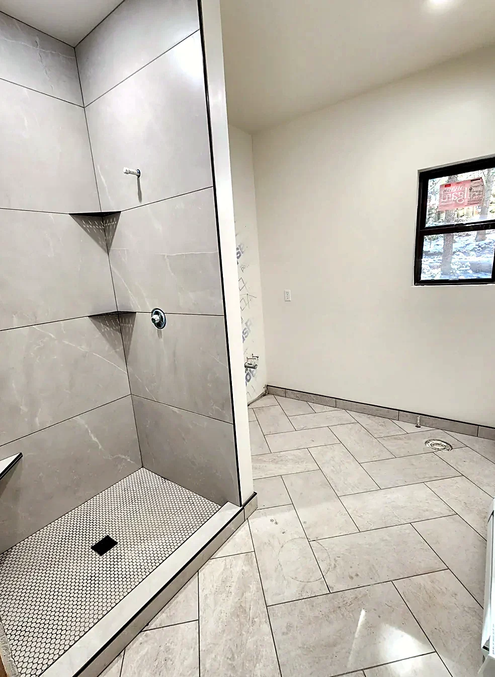 Bathroom floor in a herringbone pattern of light stone-look tile leading to a walk-in shower