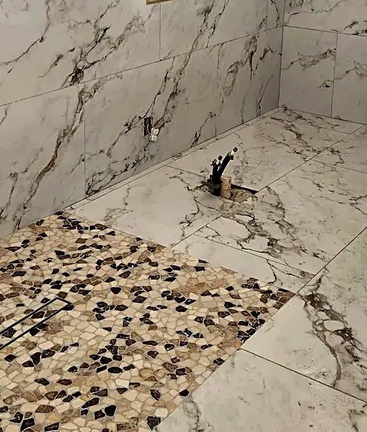 Detail of a pebble mosaic accent band meeting marble-look porcelain at a linear drain