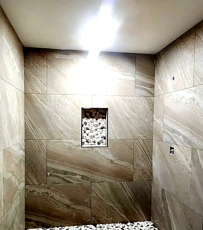Marble-look shower enclosure with a pebble mosaic pan and a recessed niche at eye height