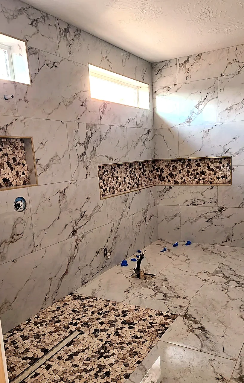 Marble-look porcelain shower with a pebble mosaic accent band running through the niche